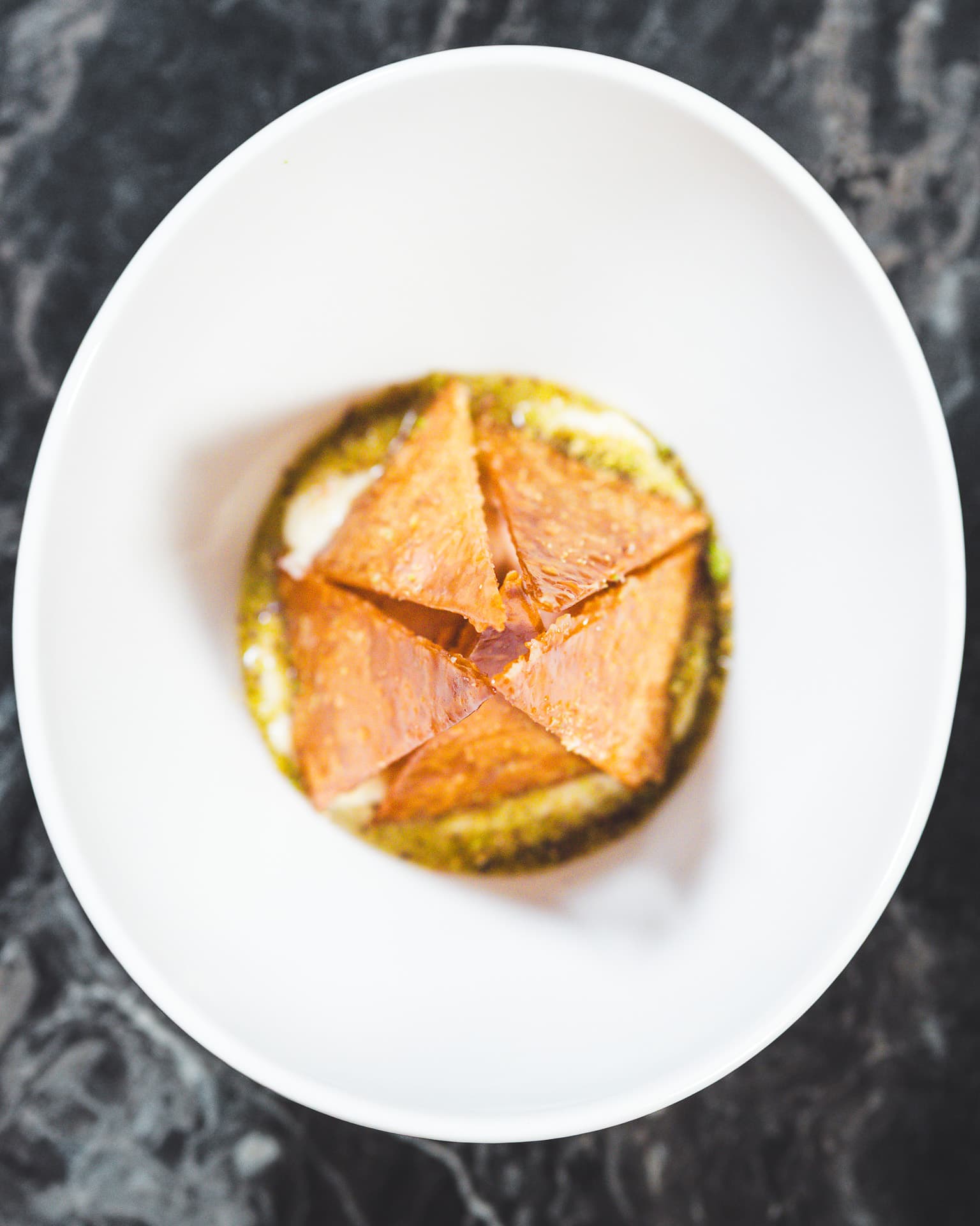 A layered pastry on a pool of green pistachio cream, seen from above.